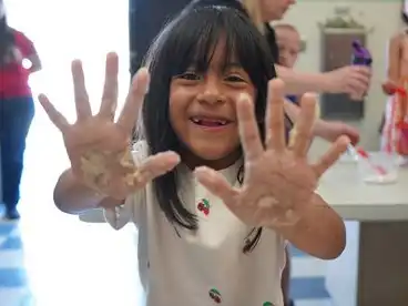 A young girl shows off dirty hands from making playdough with her parents at ArtsFest