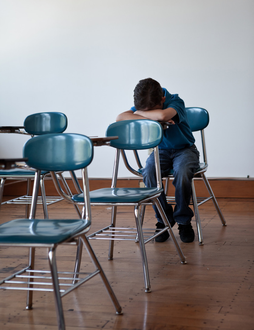 Photo of a single student sitting in an empty classroom with head down
