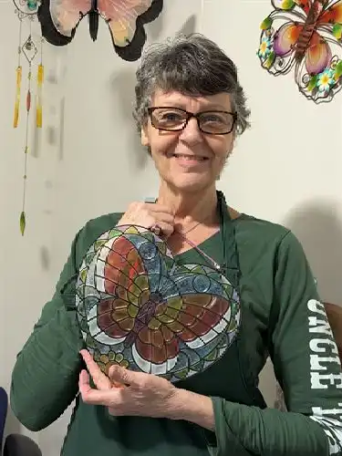 Adult in green apron holding a stained glass butterfly