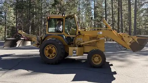 Tractor on a paved surface with a friendly adult driving amidst a forest backdrop