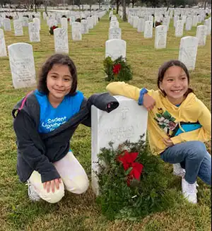 Students laying wreaths at gravestone for Wreaths Across America