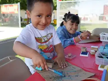A young boy smiles while he makes art on a paper bag for ArtsFest