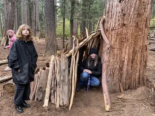 Two students squat in and outside a lean-to shelter