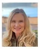 Woman with long, blonde hair smiles with blurred out lake in background