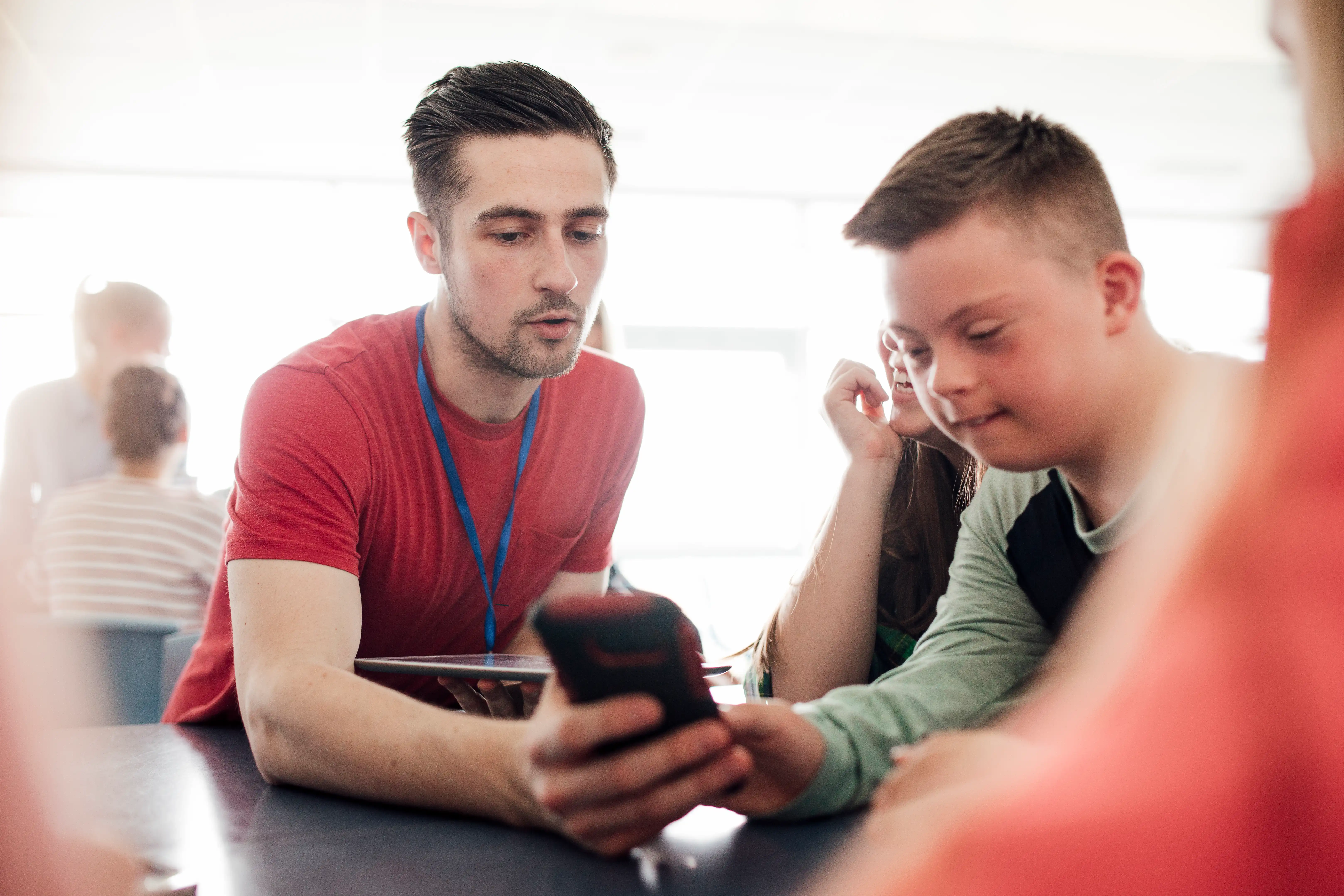 An adult sitting with a student talking and showing the student a phone screen.