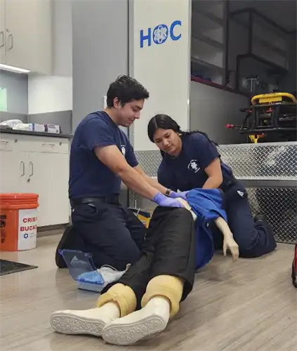 Two EMT students roll a manikin over to demonstrate how to prevent choking