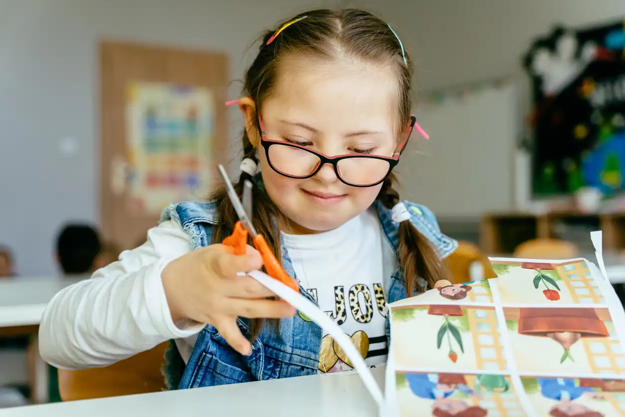 A photo of a female student with glasses using a pair of scissors to cut paper