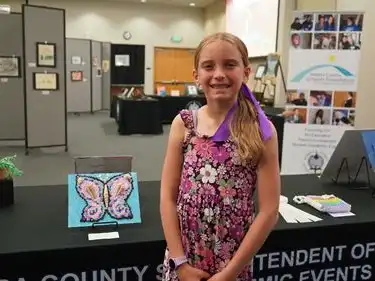 A student poses for a photo with her art in the art gallery at ArtsFest