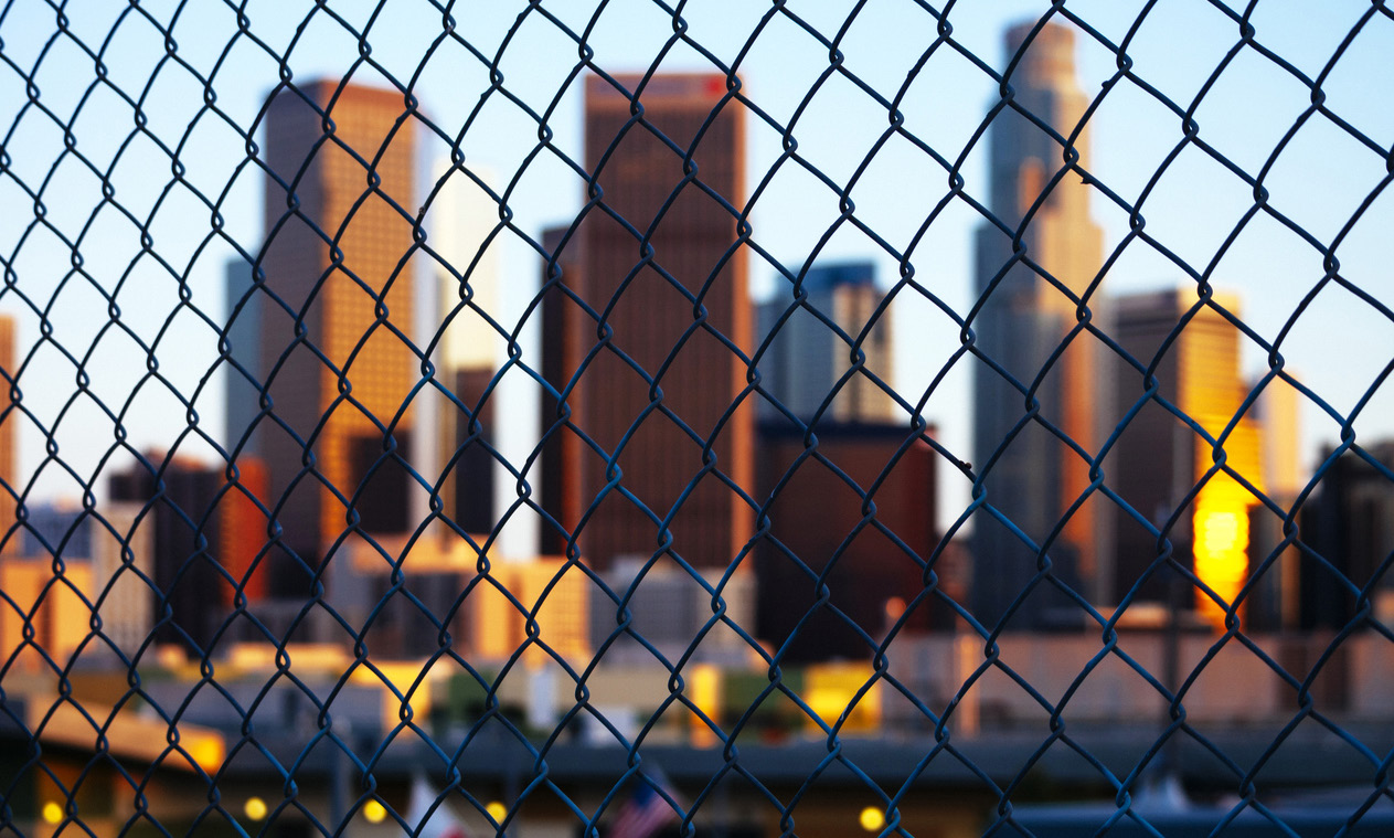 Photo of cityscape seen through a chain-linked fence.