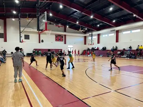 Student-athletes compete during a basketball game as families and spectators watch from the bleachers.