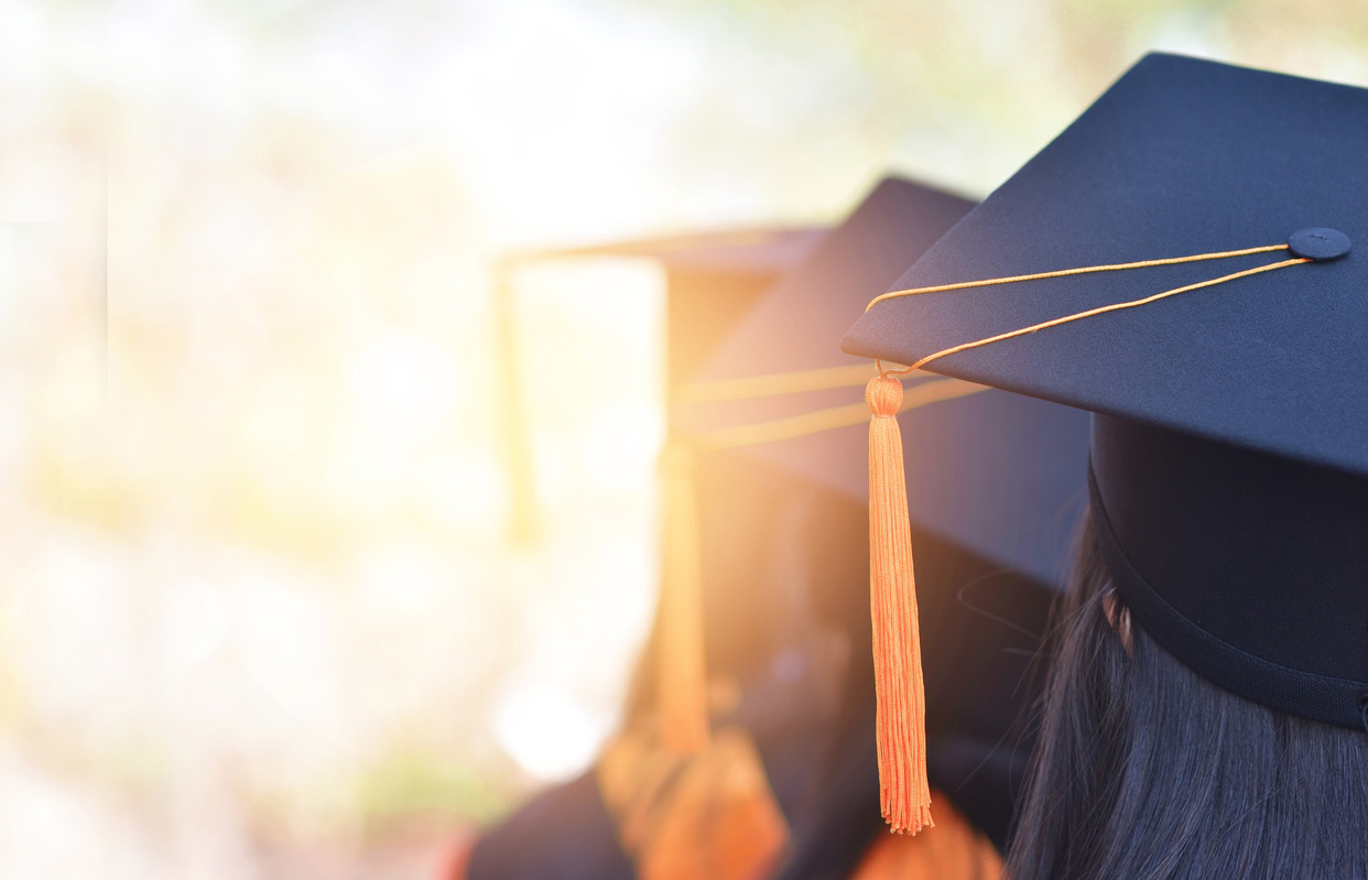 Photo of cap and gowned graduates facing bright sunlight
